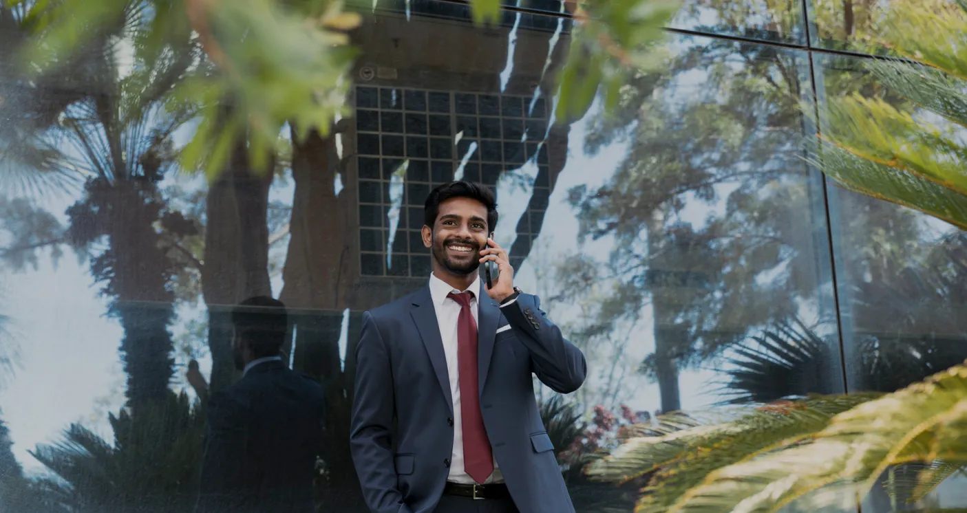 Director smiling while speaking on a phone outside a glass building